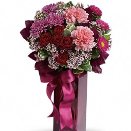 Bouquet of pink and red flowers in a tall glass vase with a ribbon