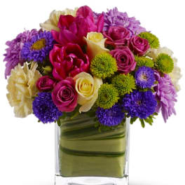 Mixed bouquet of pink, purple, white, and green flowers in a clear glass vase
