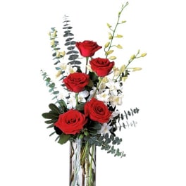 Red roses in a clear glass vase with white orchids and tall greenery