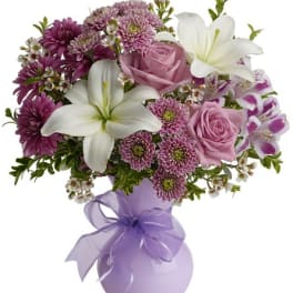 Pink and white bouquet in a lavender vase with a ribbon bow