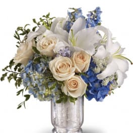 White lilies, cream roses, and blue flowers in a glass vase