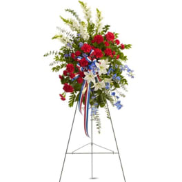 Standing floral spray with red carnations, white lilies, and blue accents on an easel
