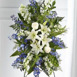 Tall standing spray of white lilies, roses, and blue flowers on a metal easel