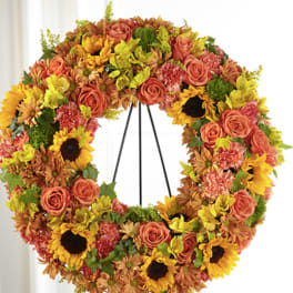 Standing floral wreath of yellow sunflowers, orange roses, and mixed warm-toned blooms on a metal easel