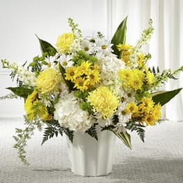 Yellow and white chrysanthemums, daisies, and hydrangeas arranged in a white vase.