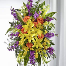Tall standing spray of yellow lilies, orange roses, and purple flowers on a metal easel
