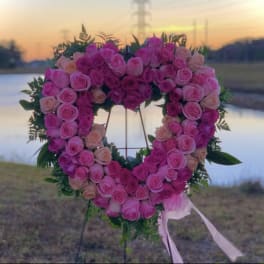Heart-shaped standing wreath of pink and peach roses on an easel with trailing ribbons outdoors at sunset