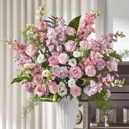 Tall arrangement of pink roses, carnations, and white flowers in a white urn on a pedestal