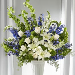 Tall white and blue arrangement with lilies, roses, delphinium and Bells of Ireland in a white pedestal vase.