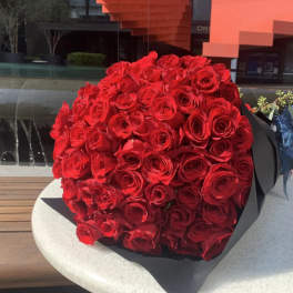 Large bouquet of tightly packed red roses wrapped in black paper with a blue ribbon