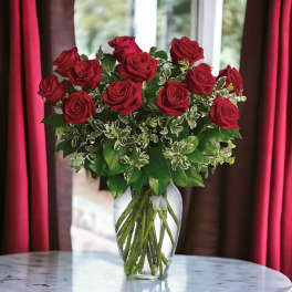 Tall arrangement of red roses in a clear glass vase on a round marble table.