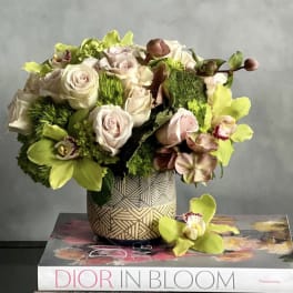 Compact arrangement of blush roses and green orchids in a patterned vase on books