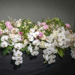 Long cascading arrangement of white orchids with pink and ivory blooms on a dark surface