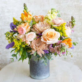 Peach and yellow mixed flower arrangement with roses and mums in a gray metal cylinder vase
