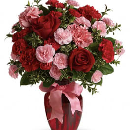Red roses and pink carnations in a red vase with a pink ribbon