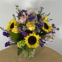 Mixed bouquet of sunflowers, yellow and pink roses in a clear glass vase
