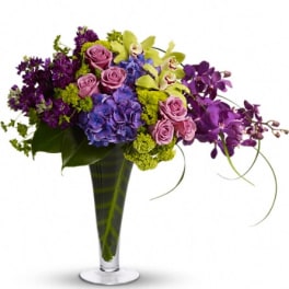 Purple and pink floral arrangement in a tall glass vase