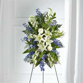 Standing floral spray with white lilies and blue flowers on an easel