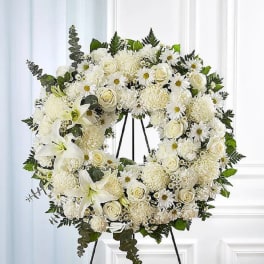 White floral wreath on a black easel with lilies and roses