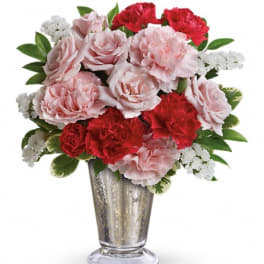 Pink and red carnations with white filler flowers in a silver vase