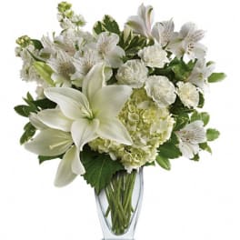 White lilies and mixed white flowers in a clear glass vase