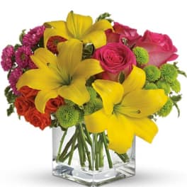 Bouquet of yellow lilies, pink roses, and green pompons in a clear glass vase