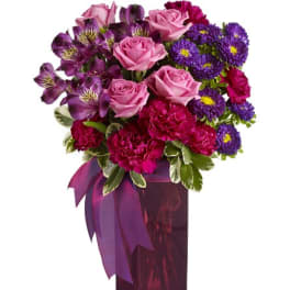 Pink roses and purple flowers in a tall magenta vase with a ribbon