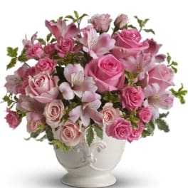 Pink roses and lilies arranged in a white pedestal vase