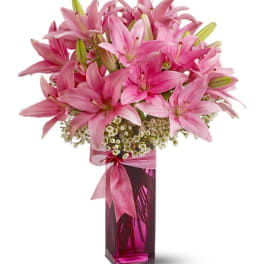 Pink lilies arranged in a tall magenta vase with a ribbon