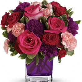 Pink and red roses with purple carnations in a purple glass vase