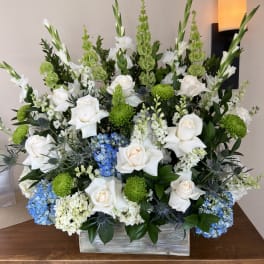 Large floral arrangement with white roses, green blooms, and blue hydrangeas in a wooden box