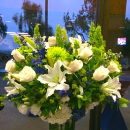 Large vase arrangement of white lilies and roses with green and blue flowers