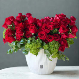 Red roses arranged in a white vase with green hydrangeas