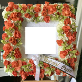 Square floral tribute with orange roses and white flowers on an easel