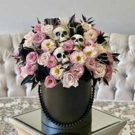 Pink and cream flowers arranged with decorative skulls in a black hatbox