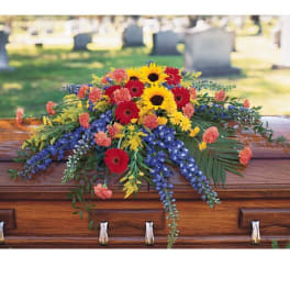 Colorful floral spray on a wooden casket with sunflowers and red daisies