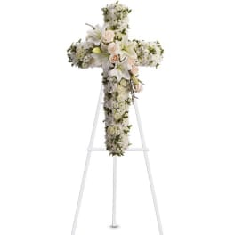 White floral cross arrangement on a stand with pale pink roses and lilies