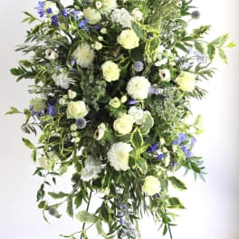Tall standing spray of white and cream flowers with blue accents arranged on a metal easel