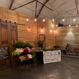 Rustic indoor flower bar setup with racks of mixed blooms and a scooter decorated with white and pink arrangements.
