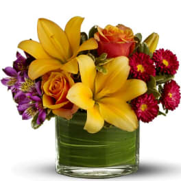 Bouquet of yellow lilies, orange roses, and purple flowers in a glass vase
