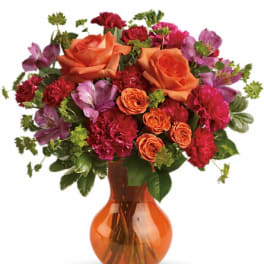 Orange and red mixed bouquet in an amber glass vase