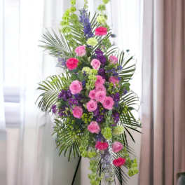 Tall standing spray with pink roses, purple flowers, and green accents on an easel.