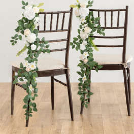 Pair of dark chairs decorated with cascading white and cream rose garlands with lush green foliage