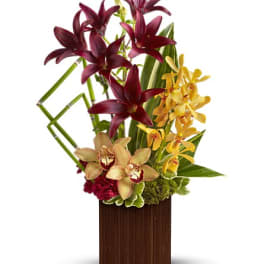 Tall orchid arrangement in a wooden vase with burgundy and yellow blooms