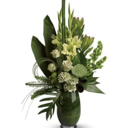 Tall green floral arrangement in a glass vase with tropical leaves and pale blooms