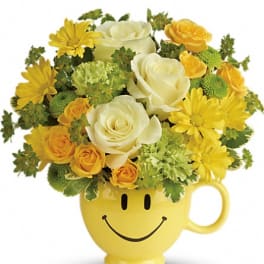 Yellow flower arrangement in a smiley-face mug