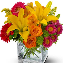 Colorful bouquet with yellow lilies, orange roses, and pink daisies in a glass vase