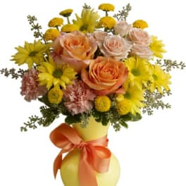 Bouquet of peach roses and yellow daisies in a yellow vase with an orange ribbon