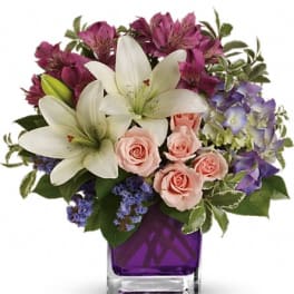 Bouquet of white lilies, pink roses, and purple flowers in a purple glass vase