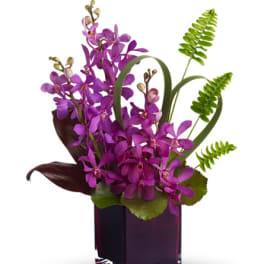 Purple orchid arrangement in a dark glass vase with green accents